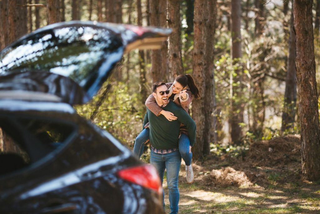 Couple walking through forest near hatchback SUV.